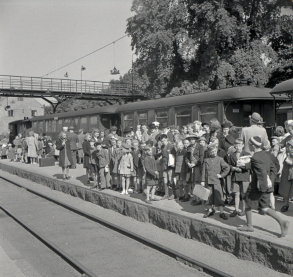 Kolonibarnen är spända av förväntan inför sommarlägret på Skrea. I bakgrunden syns gångbron över järnvägen.