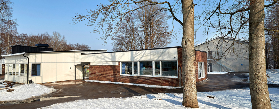 En vit och röd byggnad, framför skolan på marken ligger det snö