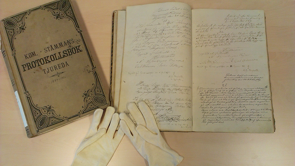 Två protokollböcker från 1800-talet och två vita handskar på ett bord.