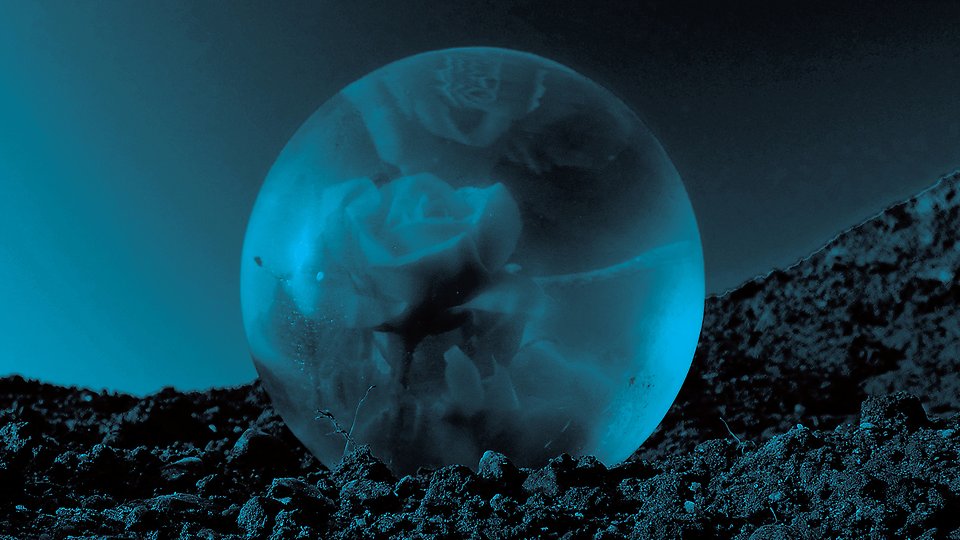 En blå glaskula som ligger på en hög med jord